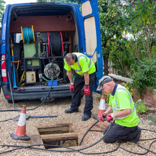 Two professional drain unblockers working on a blocked drain
